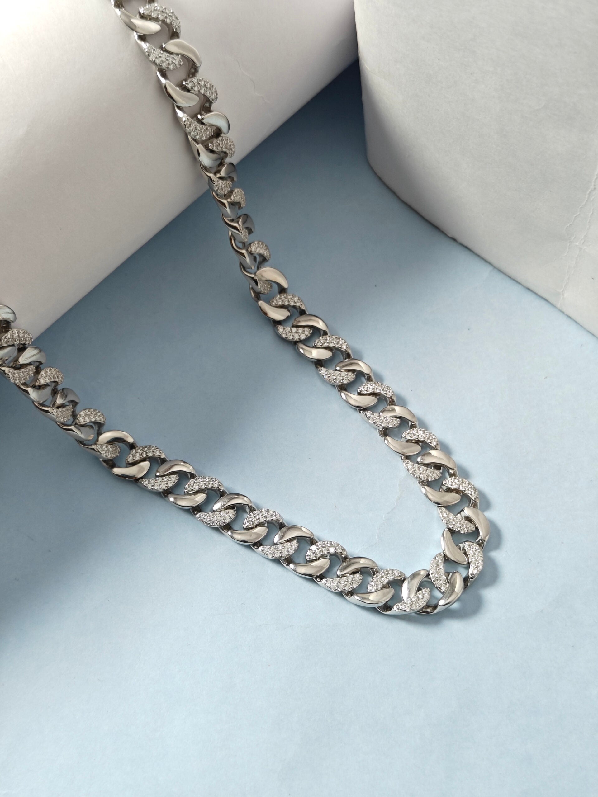 Silver chain necklace on a light blue surface with a white cushion